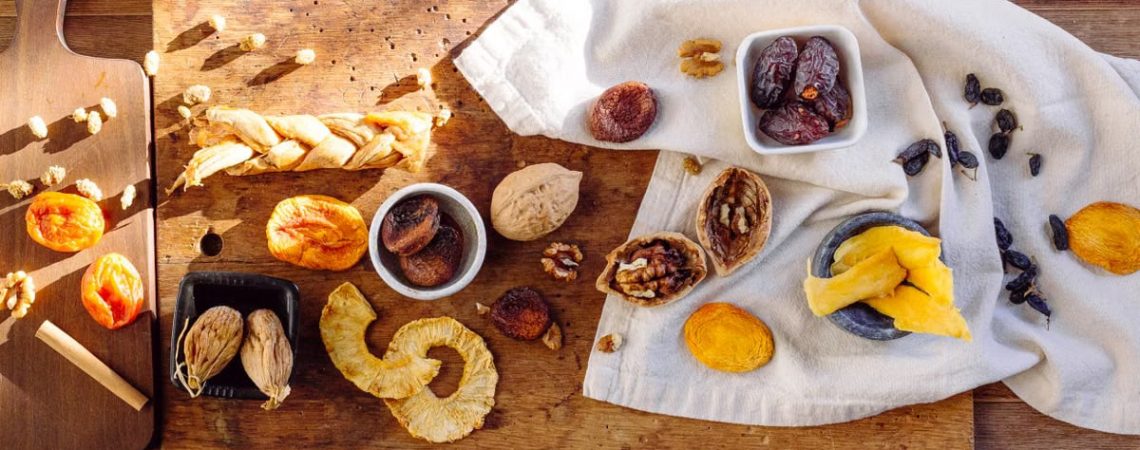 A variety of dried fruits displayed on a wooden table with cloth and cutting board.