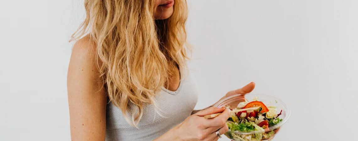 A caucasian woman in a sports bra enjoying a fresh salad, embodying healthy eating and lifestyle.